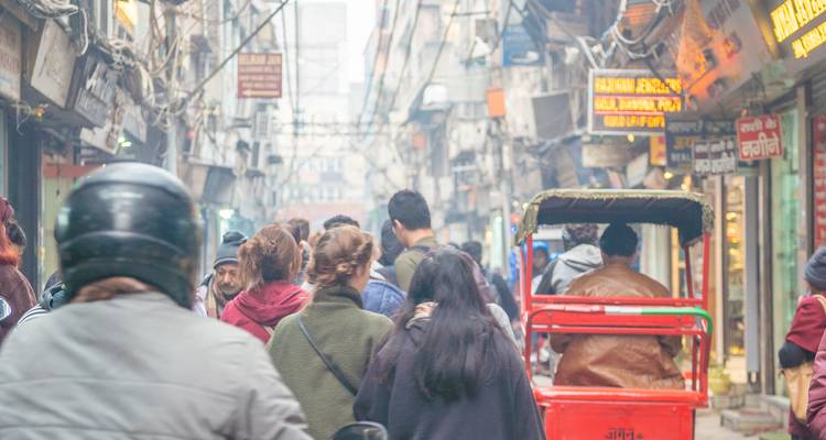 Busy street scene with people and rickshaws moving through a market area.