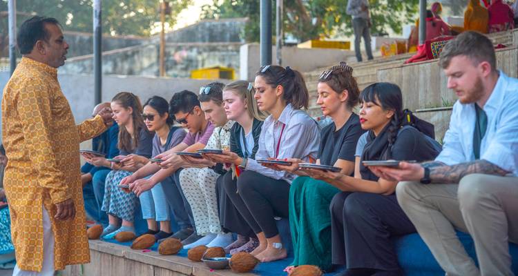 People seated on benches holding religious offerings during a ceremony.