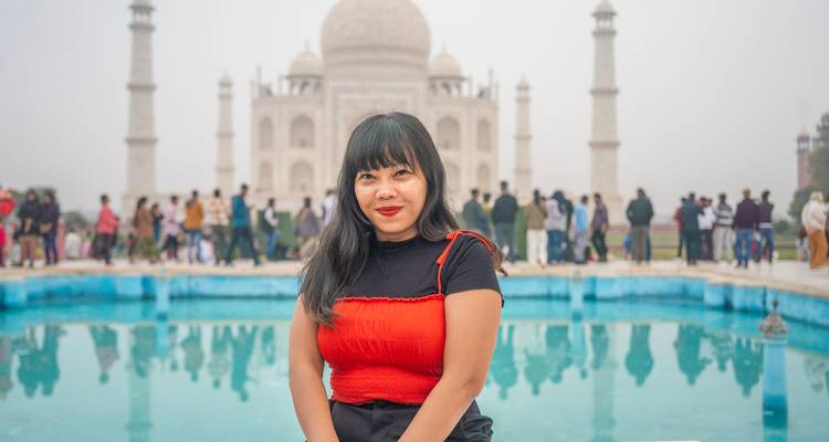 Person posing in front of the Taj Mahal, with a reflection in the pool.