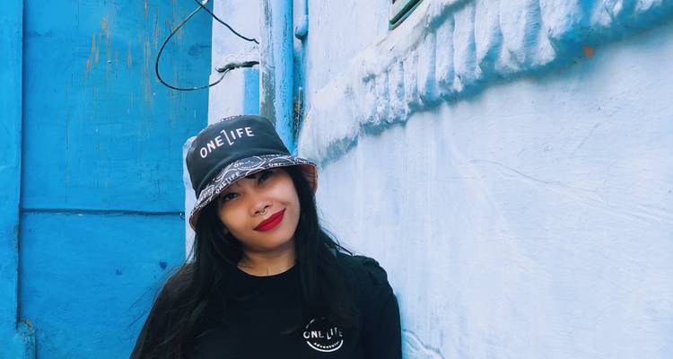 Person posing in front of a blue wall while wearing a stylish hat.