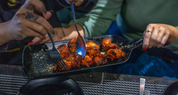 Close-up of hands sharing a dish of grilled food.