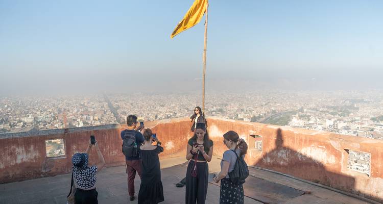Tourists taking photos with a flag on a high terrace overlooking a city.