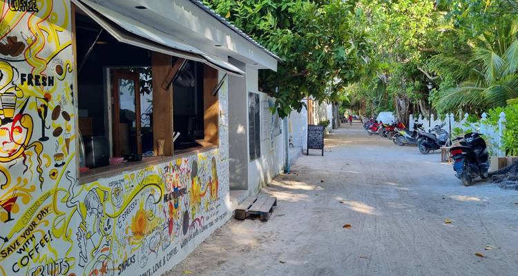 Vue de rue aux Maldives avec art mural et sentier sablonneux.
