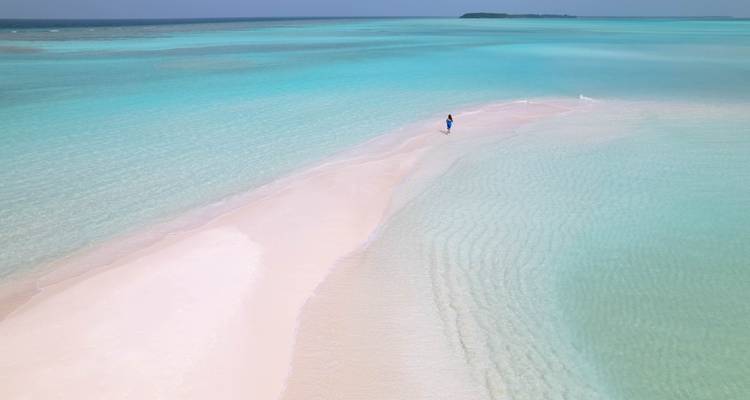 Personne marchant sur un banc de sable avec des eaux turquoise.