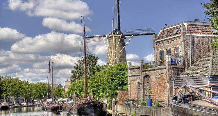 Moulin à vent historique au bord d'un canal avec des bateaux amarrés à proximité.
