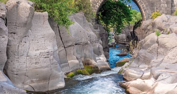 Rushing river flowing under an arch bridge amidst rocky surroundings.