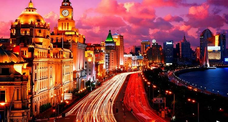 Cityscape at dusk with illuminated buildings and traffic trails.