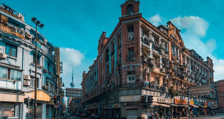Rues historiques de faible hauteur de Shanghai avec la Tour de la Perle d'Orient qui apparaît entre les bâtiments art déco pastel sous un ciel bleu.