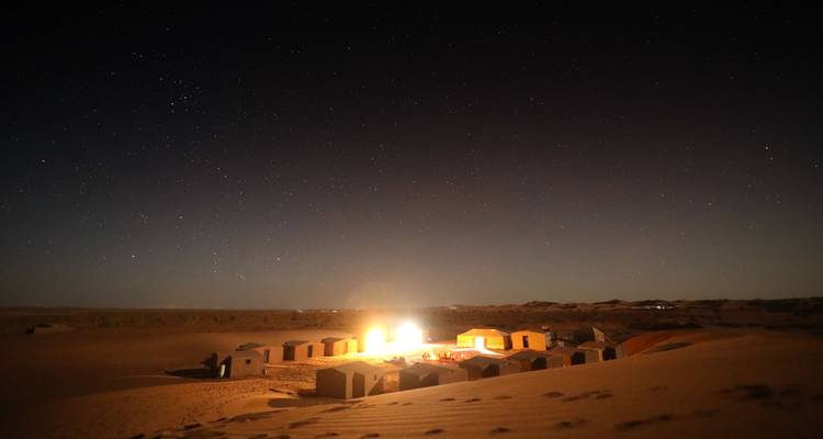 Desert campsite illuminated at night with visible constellations.