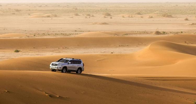 4x4 vehicle on sand dunes in a desert landscape.