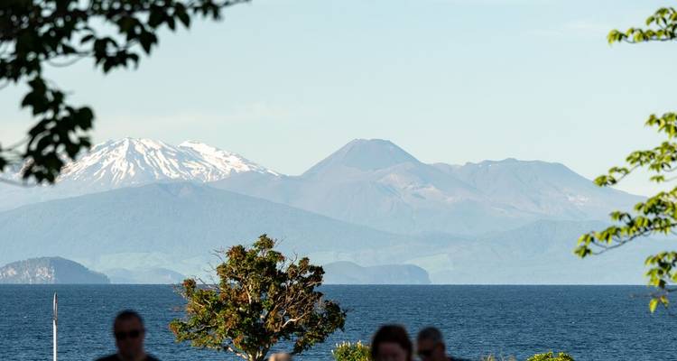 Bergketen met besneeuwde toppen zichtbaar achter een meer onder een heldere hemel.
