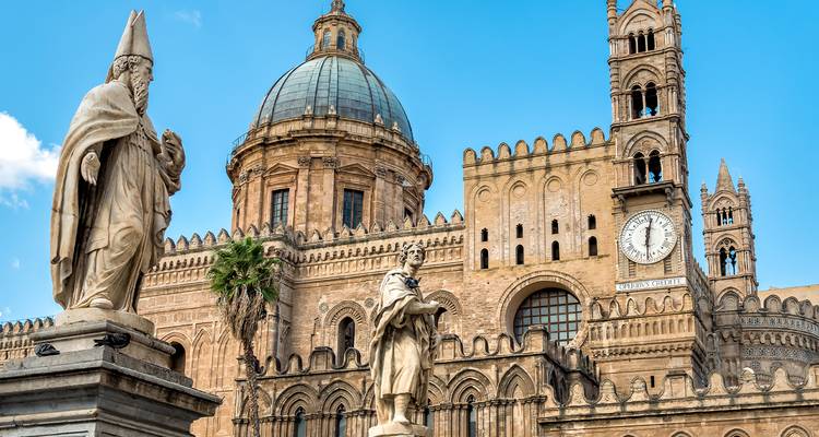 Catedral con estatuas y torre del reloj bajo un cielo despejado.