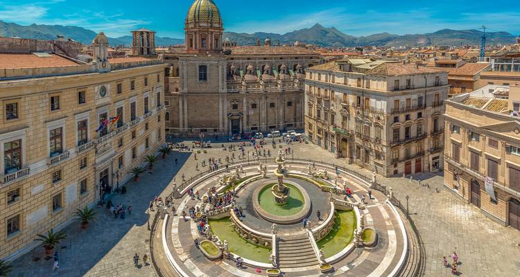 Vista aérea de una plaza de la ciudad con una fuente y edificios históricos.
