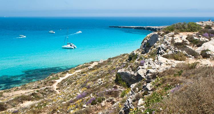 Une mer bleue claire avec des bateaux près d'un rivage rocheux sous un ciel lumineux.