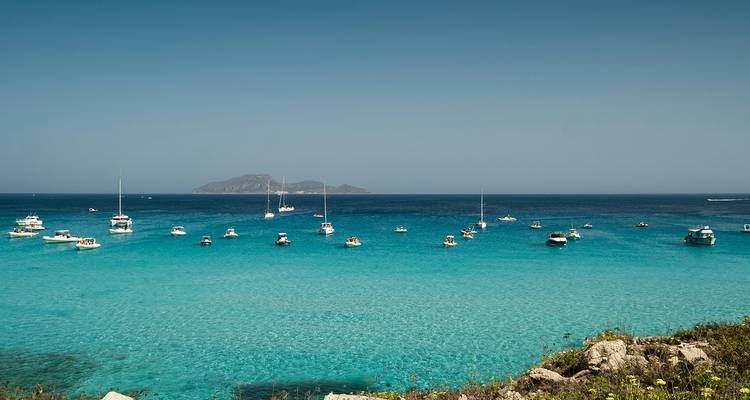 Bateaux ancrés dans les eaux bleu clair d'une plage méditerranéenne.