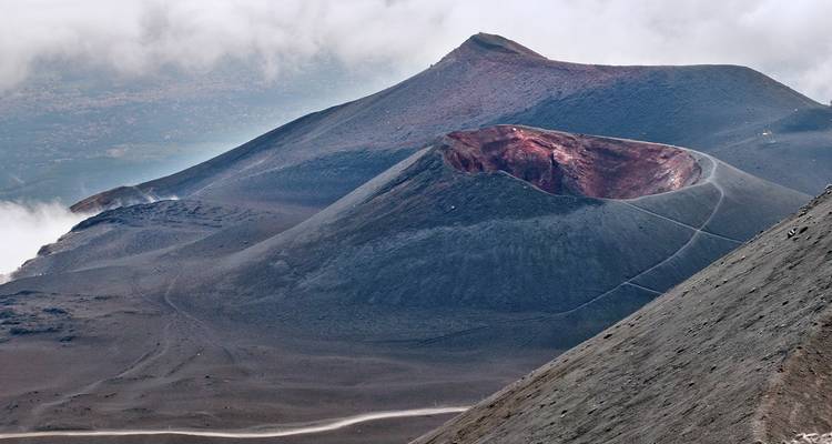 La cima de una montaña volcánica con un cráter rojo y senderos de ceniza.