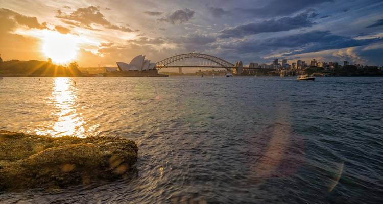 Vue du coucher de soleil sur l'Opéra de Sydney et le Harbour Bridge au-dessus de l'eau.