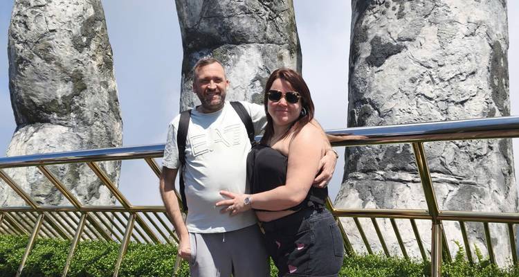 Couple souriant posant devant les sculptures géantes de mains en pierre de Ba Na Hills sur le Pont Doré