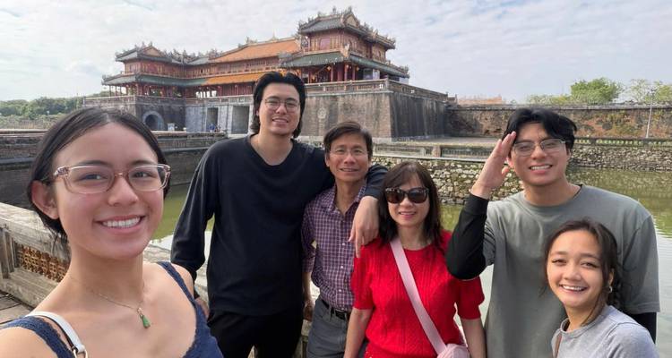 Des amis souriants se tiennent ensemble au bord des douves de la citadelle de Hué avec la porte impériale en arrière-plan.