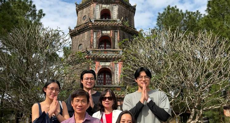 Groupe familial posant les mains jointes devant la pagode Thien Mu entourée d'arbres dépouillés.