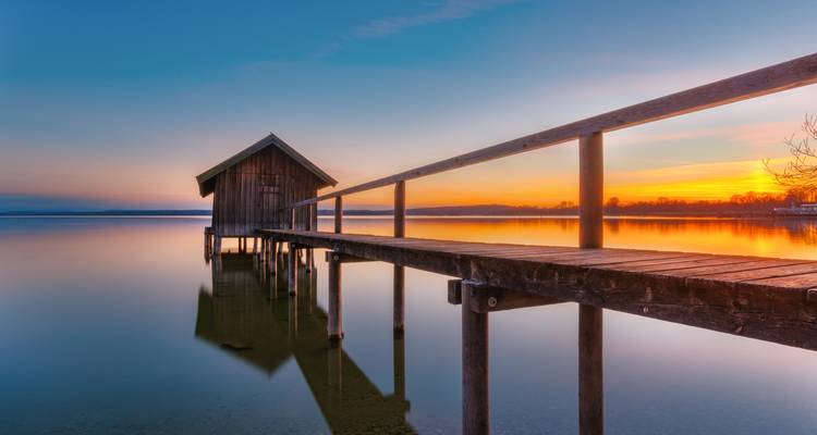 Sunset over a serene lake with a wooden pier.