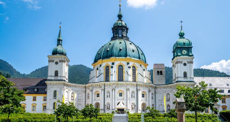 Baroque church under a blue sky with surrounding greenery.