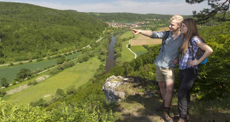 A couple pointing into the distance while standing on a cliff.