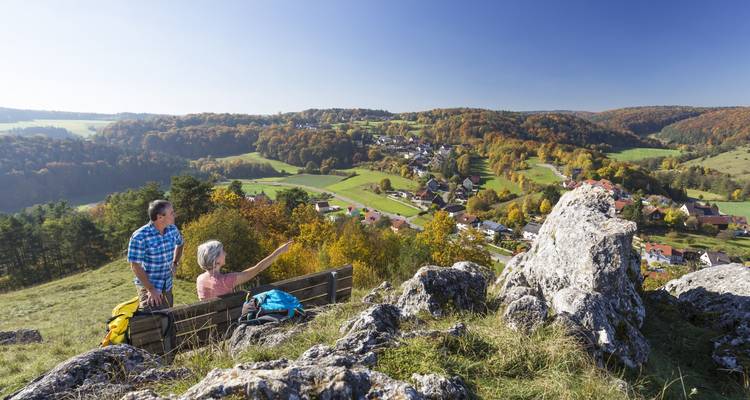 Elderly couple sitting on a bench enjoying a panoramic view of a village.