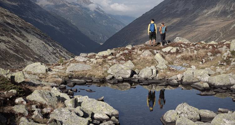 Deux randonneurs surplombant une vallée avec un petit bassin d'eau.