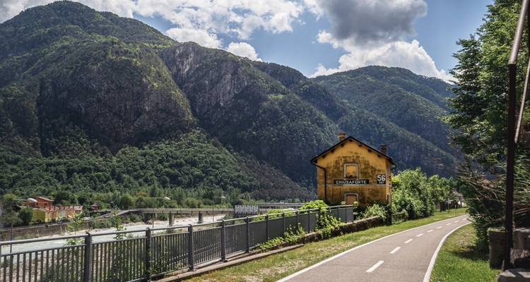 Vue panoramique de montagne avec une petite maison et une rivière.
