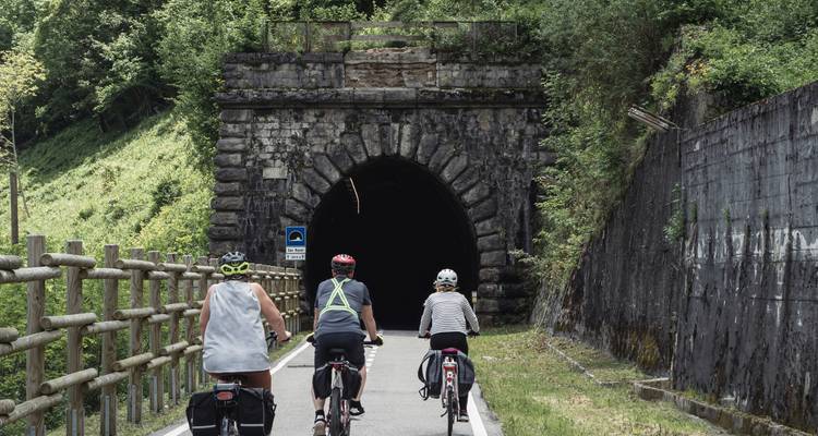 Des cyclistes entrant dans un tunnel sur une route de montagne pittoresque.