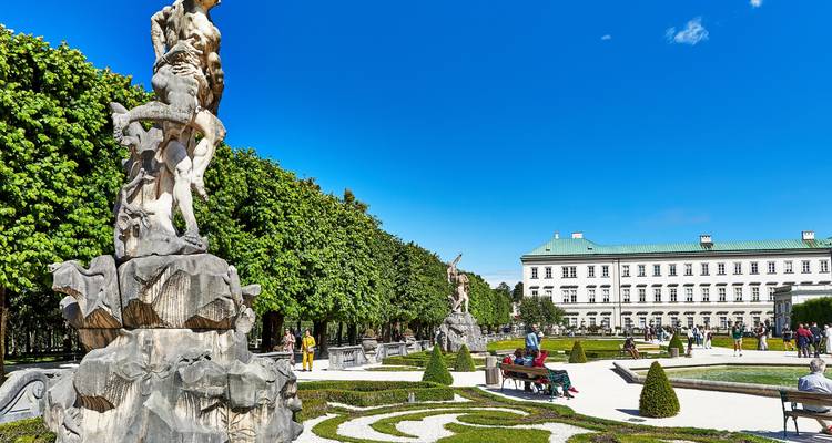 Jardin avec des statues et des haies taillées, avec des personnes qui se promènent.