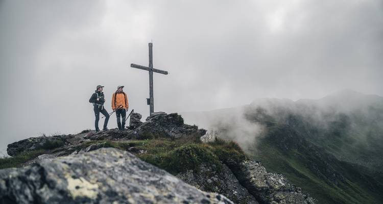 Deux randonneurs sur un sommet de montagne brumeux se tenant à côté d'une croix.