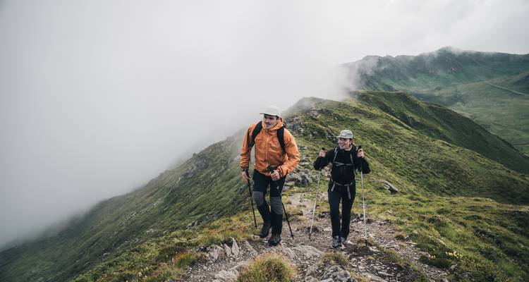 Deux randonneurs marchant le long d'une crête de montagne couverte d'herbe et de brume.