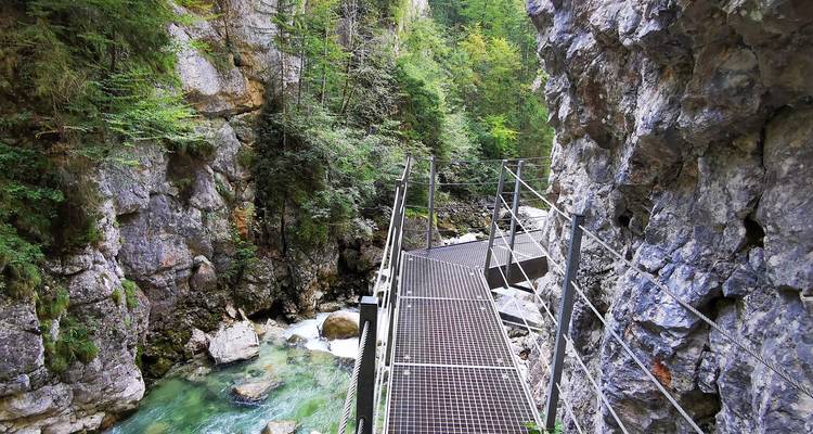 Passerelle métallique le long d'une gorge rocheuse avec un ruisseau en contrebas.