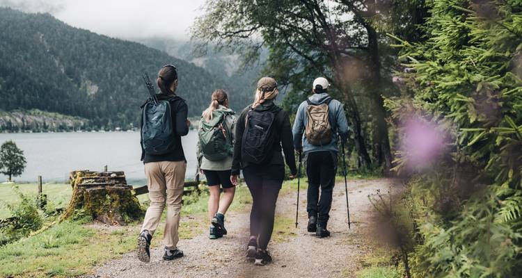 Quatre personnes en randonnée sur un sentier avec un lac en arrière-plan.