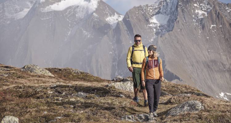 Deux randonneurs sur un sentier de montagne avec des pics enneigés en arrière-plan.