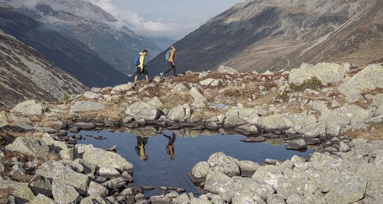 Deux randonneurs marchant près d'un étang réfléchissant dans une région montagneuse.