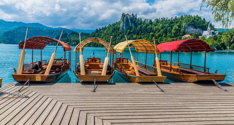 Rowboats docked by a scenic lake with a castle in the background.