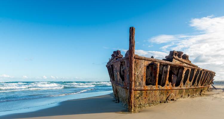 Old rusty shipwreck on a sandy beach against a clear sky.