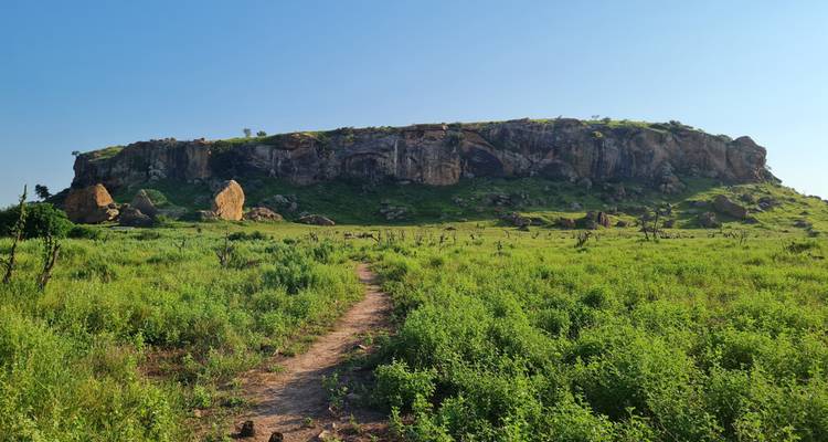 Een rotsachtige uitstulping die oprijst uit groene vlaktes met een pad dat ernaartoe leidt.
