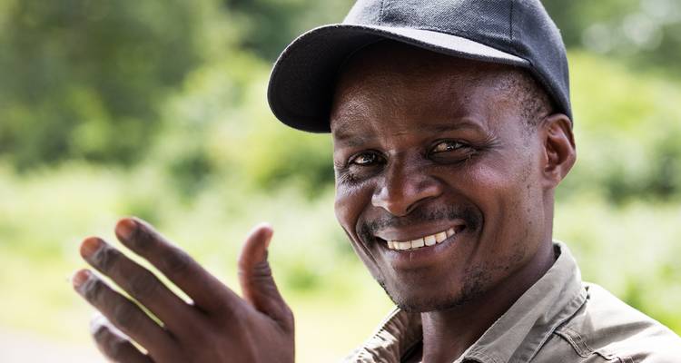 Een man die glimlacht en gebaart met een bosachtige achtergrond.