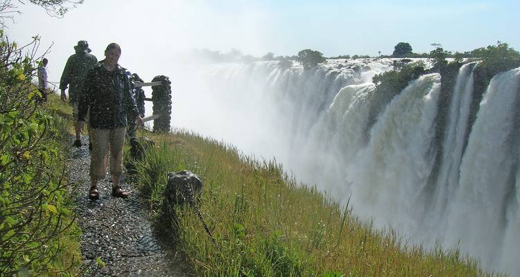 Toeristen op een mistig pad naast de Victoriawatervallen.