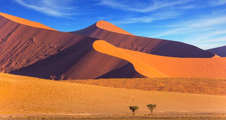 Dramatic sand dunes with vibrant colors under a blue sky.