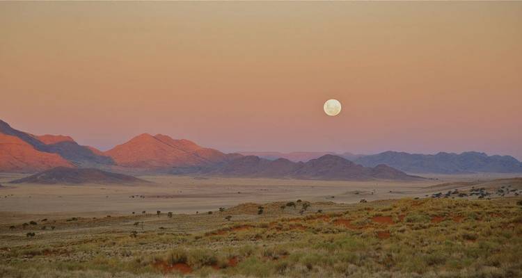 Moonrise over a desert landscape with mountains.