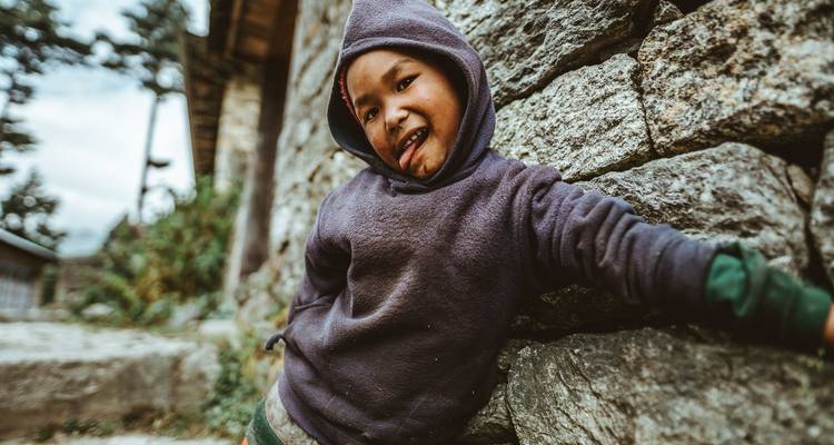 Kind in casual kleding leunend tegen een stenen muur.