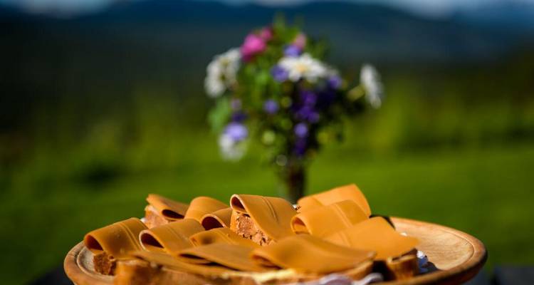 Assiette avec tranches de fromage brun sur un fond de montagne.