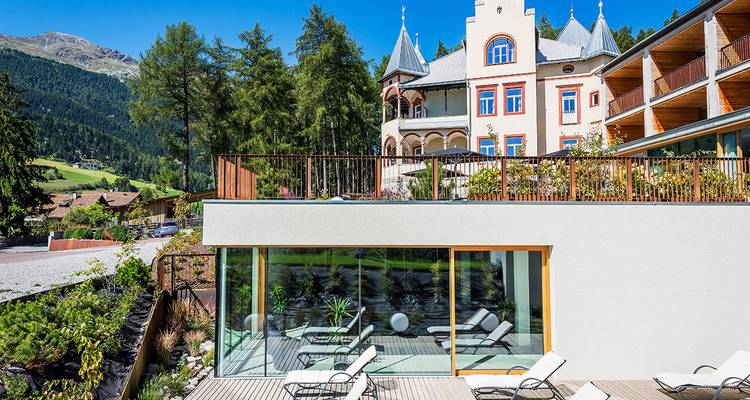 Modern hotel with glass facade set against lush hills.