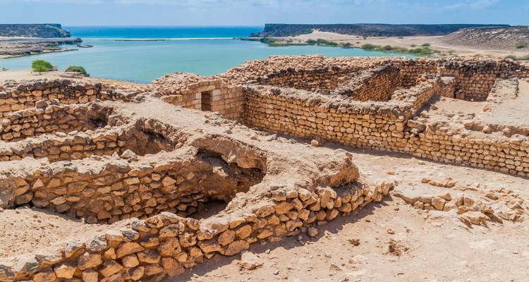 Ruins overlooking a scenic bay with clear blue water under a bright sky.