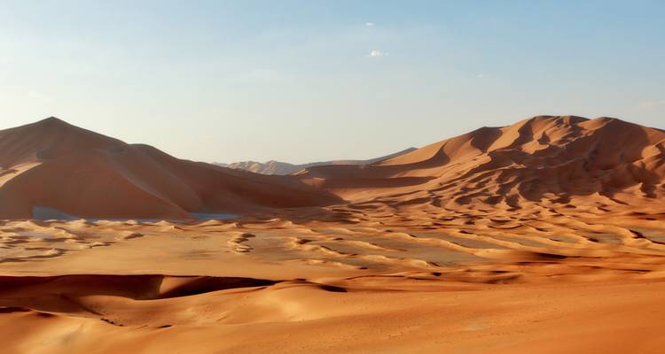 Wide landscape of sand dunes under a clear blue sky.